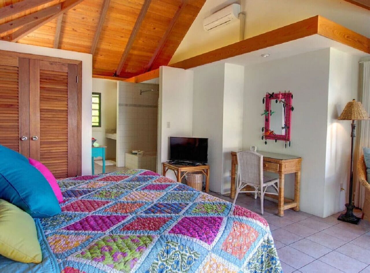 Un dormitorio con techo de madera, colcha colorida, televisor, escritorio y una silla.
