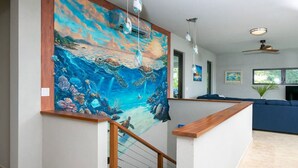 A modern interior with a large mural of sea turtles, a wooden staircase, and a blue sofa in a living area. - Tropical Seabreeze- Pool and back up power/solar (Cruz Bay)