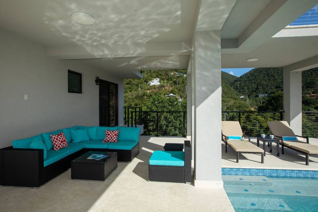 Un área de descanso al aire libre moderna con sofá y sillones, piscina y vistas a un paisaje montañoso.