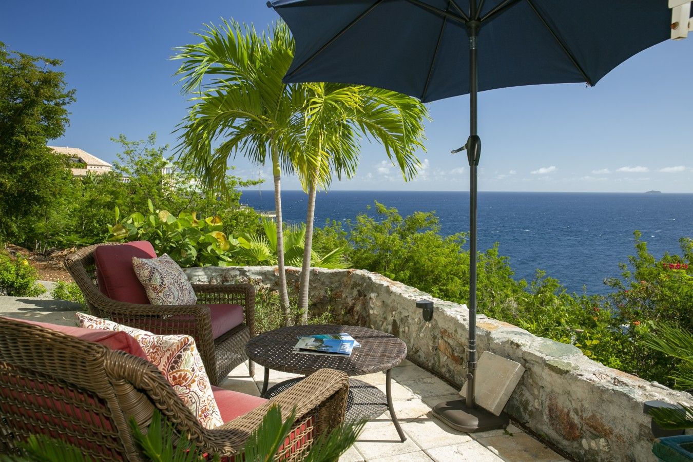 A patio with wicker furniture, a table, and an umbrella, overlooking a coastal view.