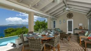 Un'area pranzo all'aperto riparata, con vista sull'oceano, arredata con sedie in vimini e un tavolo di legno apparecchiato per un pasto.