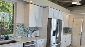Una cucina moderna con mobili bianchi, elettrodomestici in acciaio inossidabile e un'ampia finestra che si affaccia sul verde.