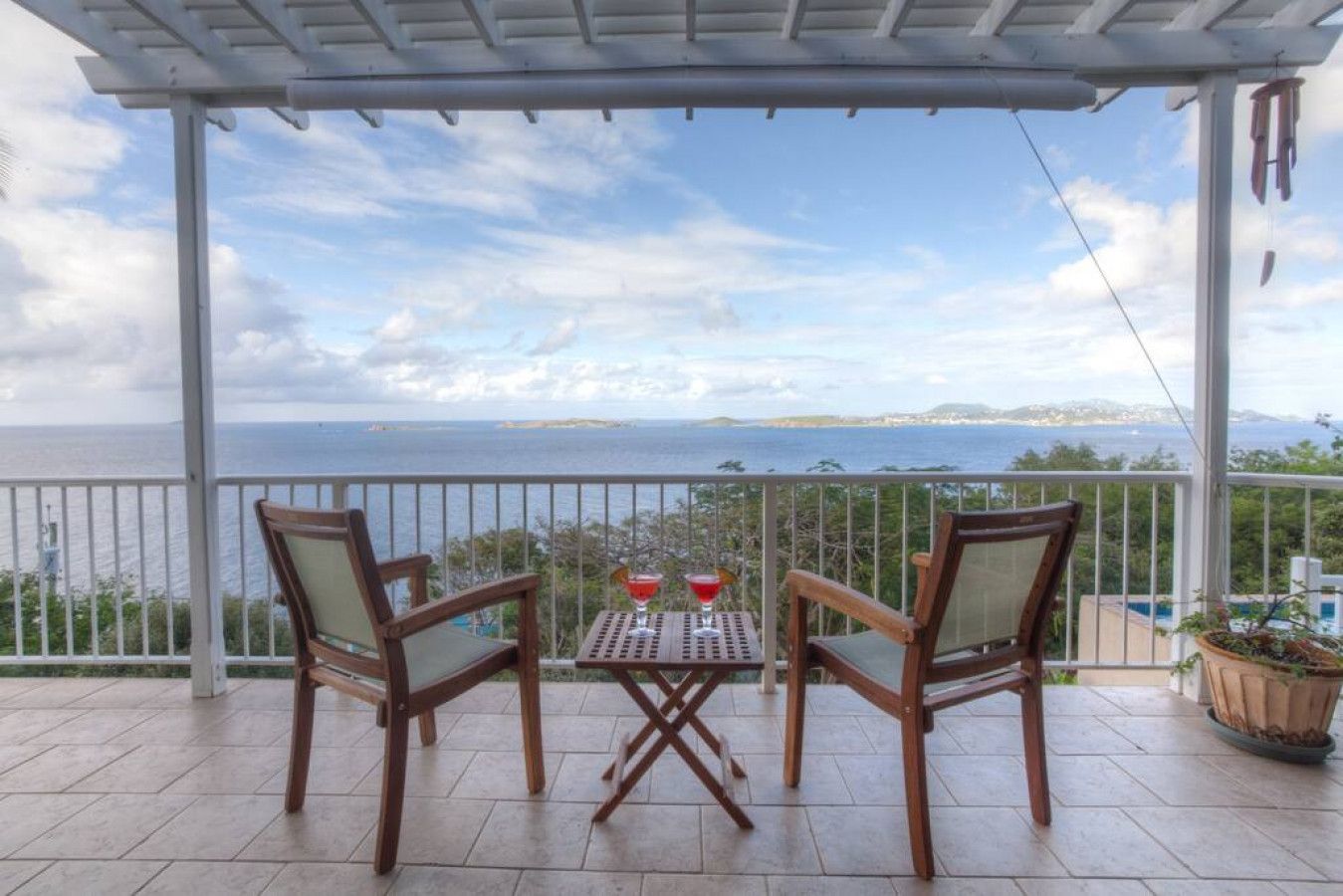 A covered balcony with two wooden chairs and a small table, overlooking a scenic view of the sea and distant land.