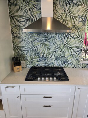 A kitchen with a gas stove, white cabinets, and a leaf-patterned backsplash.