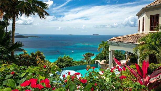 A coastal view with a clear sky, a swimming pool, and a building with a tiled roof.