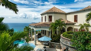 A two-story building with a tiled roof, a pool, and outdoor seating.