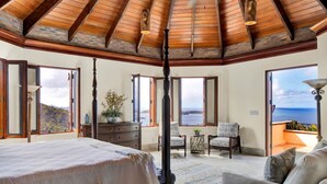 A bedroom with a large bed, a ceiling fan, and a view of the ocean through the windows.