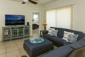 A living room with a sofa, a television on a cabinet, a lamp, and a view of a bedroom through a doorway.