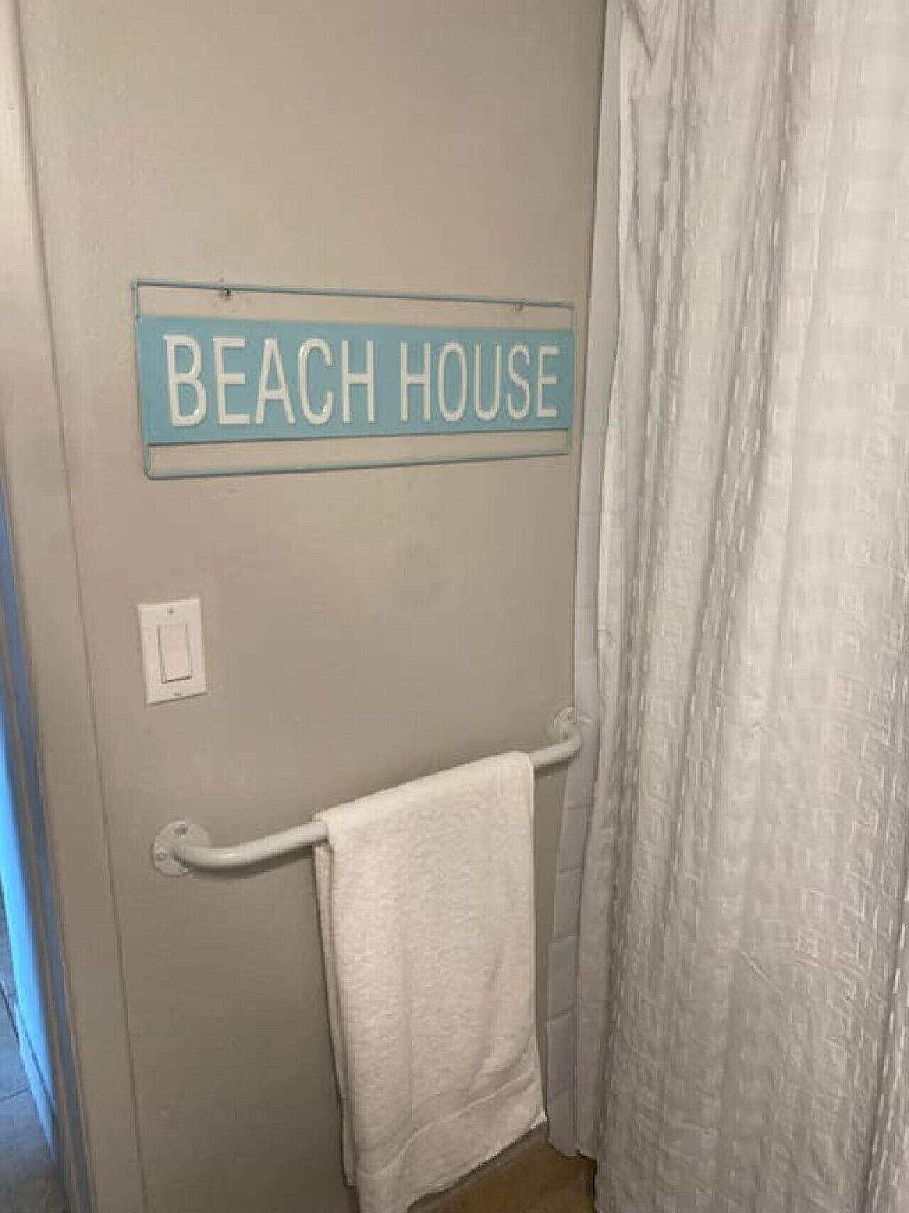 Un baño con un perchero, un letrero que dice "BEACH HOUSE" y una cortina de ducha.