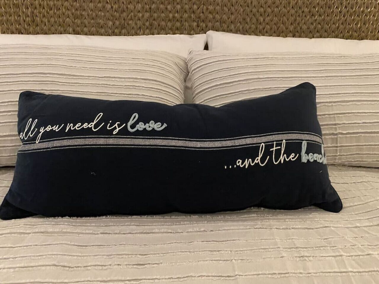 Un cojín negro con texto blanco sobre una cama con ropa de cama a rayas.
