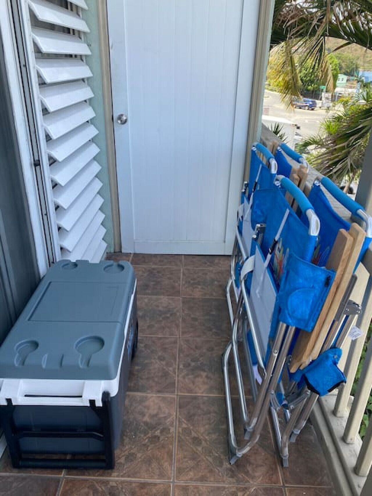 A small room with a white door, a window with blinds, a blue cart with a blue bag, and a grey object on the floor.