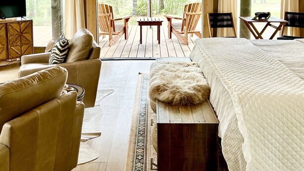 A tented room with a bed, a TV, and seating area with chairs and a table.