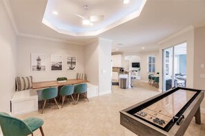 A modern living room with a pool table, a dining area with chairs, and a kitchen in the background.