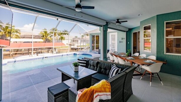 An indoor pool area with a sofa and dining table, large windows, and a ceiling fan. - Dolphins Cove (Cape Coral)