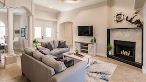A modern living room with a grey sofa, a coffee table, a flat-screen TV, and a fireplace. - Dolphins Cove (Cape Coral)