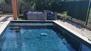 Ein rechteckiger Swimmingpool mit klarem, blauen Wasser, umgeben von einer gefliesten Terrasse und einer Rasenfläche.