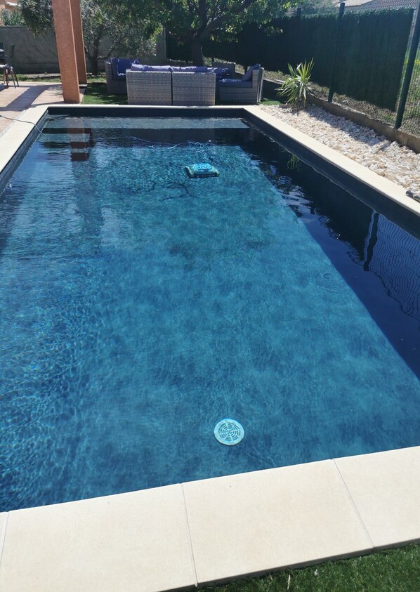 A rectangular swimming pool with clear blue water, surrounded by a tiled deck and a grassy area.