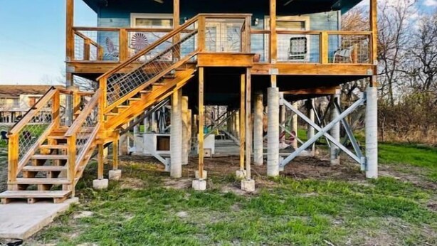 Edificio in legno a due piani con tetto blu, una scala che conduce al livello superiore e un’area recintata.