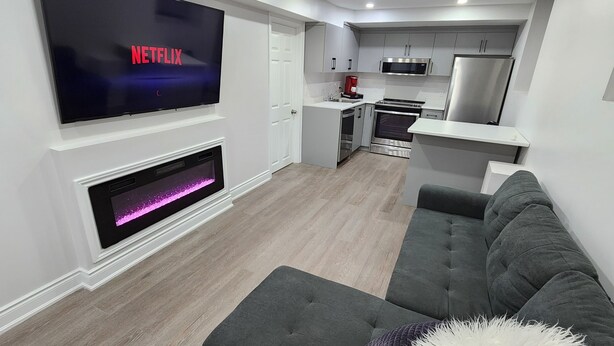 Una sala de estar moderna con televisor de pantalla plana, chimenea, sofá gris y una cocina con electrodomésticos de acero inoxidable.