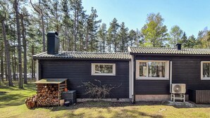 Eine Holzhütte mit Schornstein, einer kleinen Veranda und einem Holzstapel.