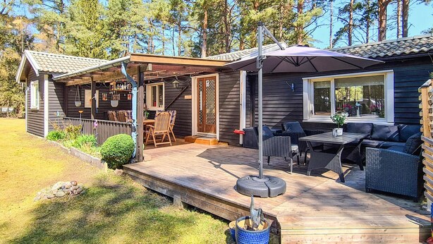 Eine Holzterrasse mit Gartenmöbeln, ein überdachter Patio-Bereich und Blick auf ein bewaldetes Gebiet.