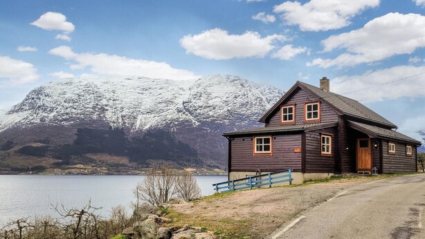 En træhytte med mørkt tag, skorsten og nummer '616' på døren. Den ligger ved et vandløb med et bjerg i baggrunden.