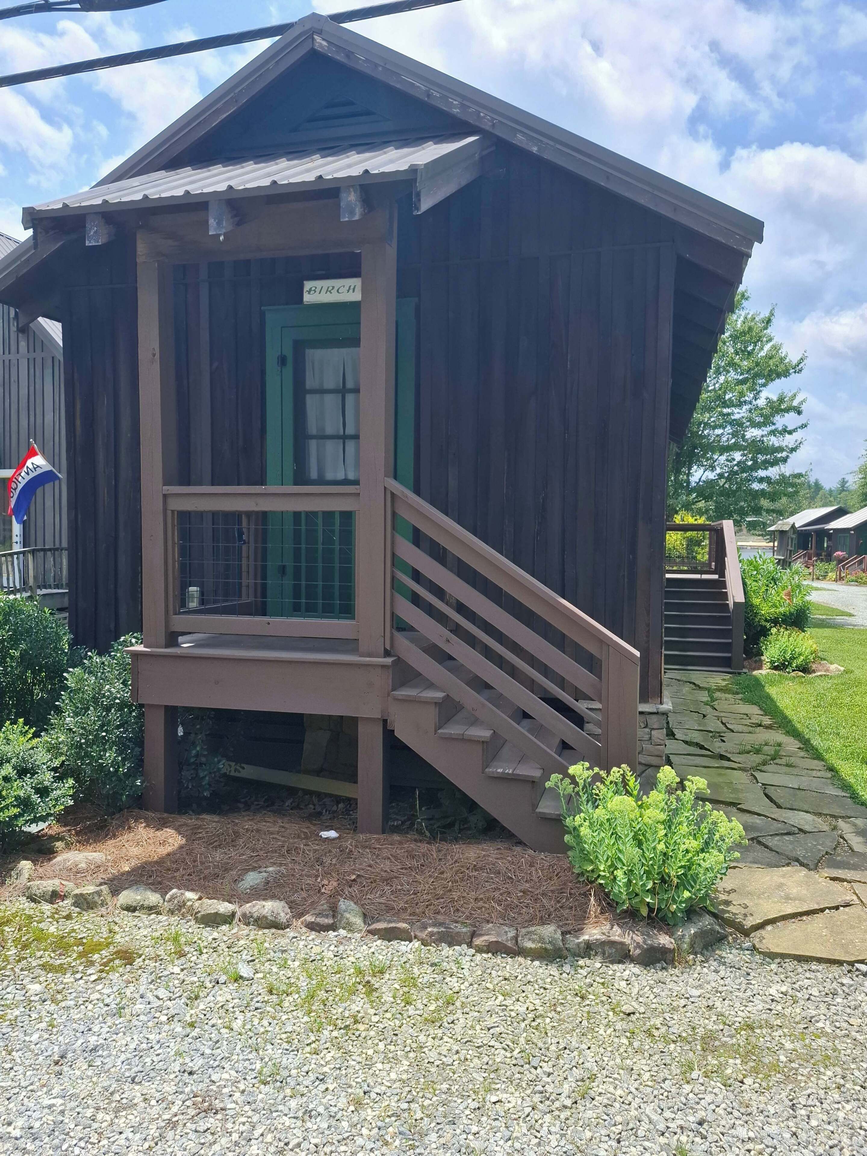 A wooden cabin with a porch, a staircase, and a sign that reads 'BIRCH'.
