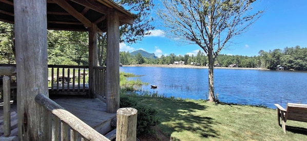 A wooden deck with a view of a lake, a bench, and a tree.