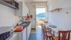 Une cuisine compacte avec vue sur la mer, un coin repas avec des chaises en bois et un ventilateur de plafond.