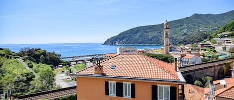 A coastal town with terracotta-roofed buildings, a prominent clock tower, and a clear view of the sea.