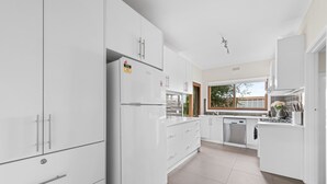 A modern kitchen with white cabinetry, a built-in dishwasher, and a window providing natural light. - Beautiful Victorian Home With Amazing Views and Centrally Located (Portarlington)