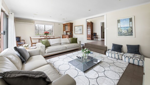 A spacious living room with a large sofa, a coffee table, and a dining area with wooden cabinets and a view of the outdoors. - Beautiful Victorian Home With Amazing Views and Centrally Located (Portarlington)