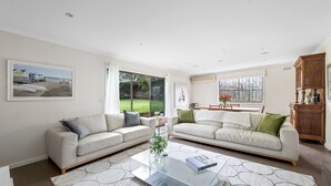 A spacious living room with two sofas, a glass coffee table, and a view of the backyard. - Beautiful Victorian Home With Amazing Views and Centrally Located (Portarlington)