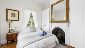 A bedroom with a bed, a nightstand, a lamp, a framed picture, a window with curtains, a fireplace, and a large mirror. - Beautiful Victorian Home With Amazing Views and Centrally Located (Portarlington)
