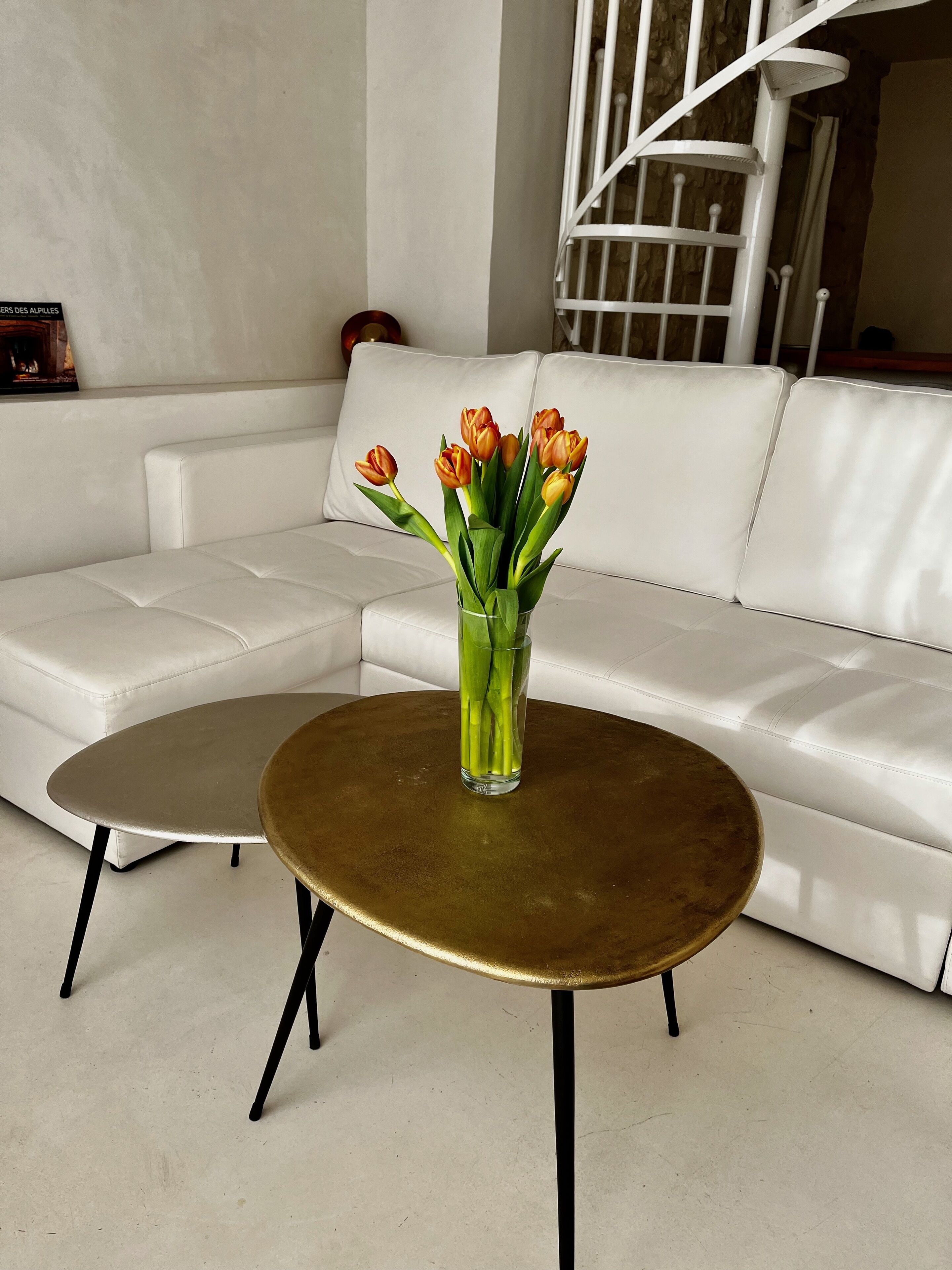 A white leather sofa, a round gold table, and a clear glass vase with orange tulips.