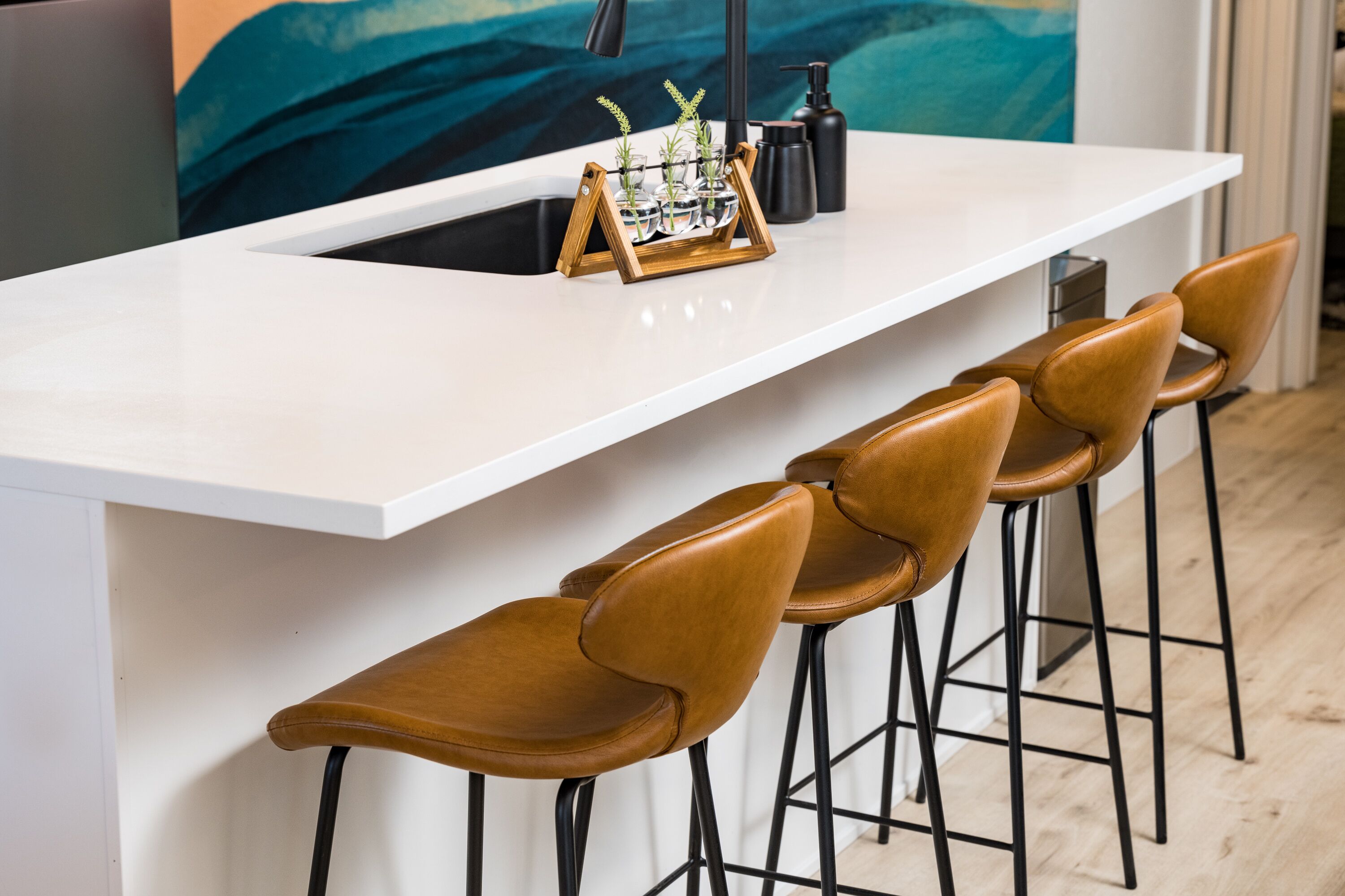A modern kitchen with a white countertop, a sink, and a bar area with four stools.