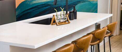 A modern kitchen with a white countertop, a sink, and a bar area with four stools.