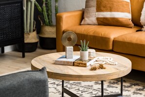 Ein runder Couchtisch aus Holz mit Büchern, einem dekorativen Metallgegenstand, einer kleinen Topfpflanze und einer Lichtschnur mit weißen Perlen.
