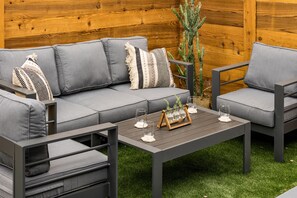 Ein moderner Außenbereich mit einer grauen Couch und passenden Sessel, einem Holztisch und einer Kakteenpflanze.