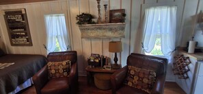 A room with two leather armchairs, a small table with a lamp, and a shelf with decorative items.