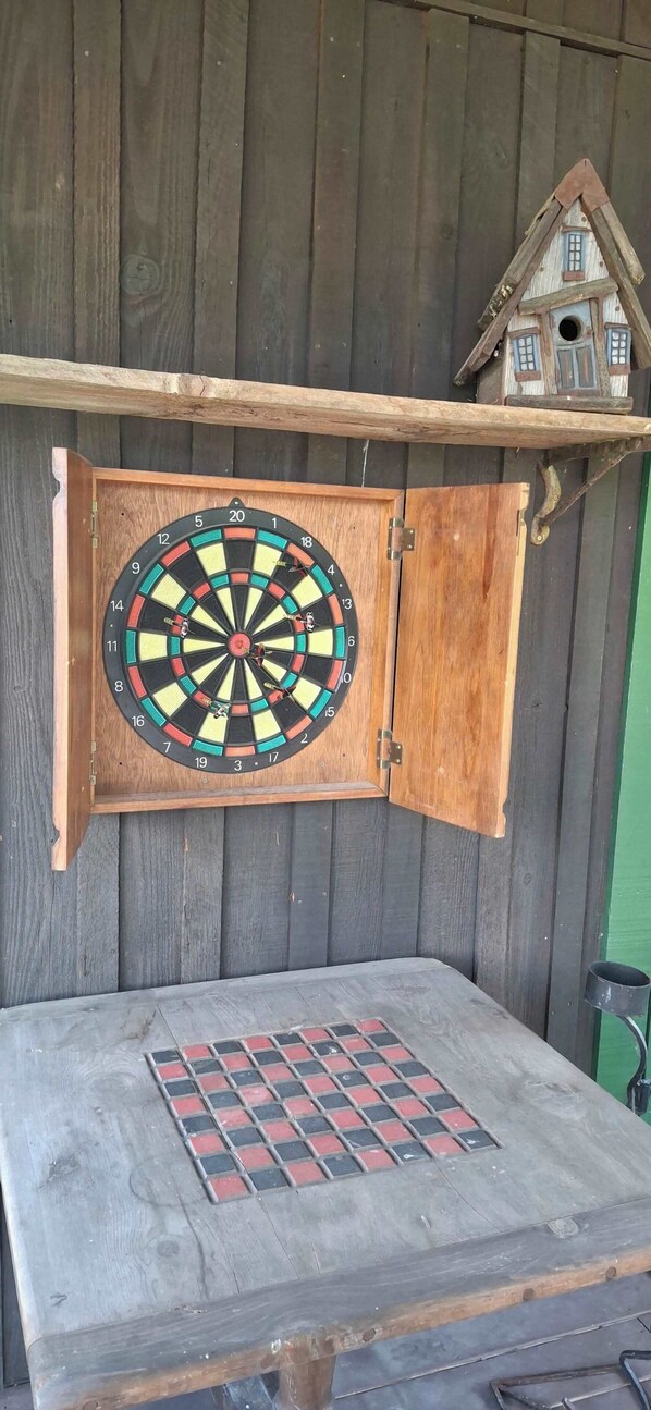 A dartboard mounted on a wooden cabinet with a green wall in the background. - The Buckeye | Lakefront Porch at Cashiers Lake (Cashiers)