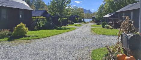 Camí de grava que condueix a una filera de cabanes, amb un llac i muntanyes al fons.