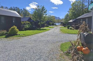 A gravel road leading to a row of cabins with a lake and mountains in the background. - The Hemlock | Pet-Friendly Fall Retreat (Cashiers)