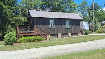 A wooden cabin with a metal roof, a wooden deck, and a gravel driveway.