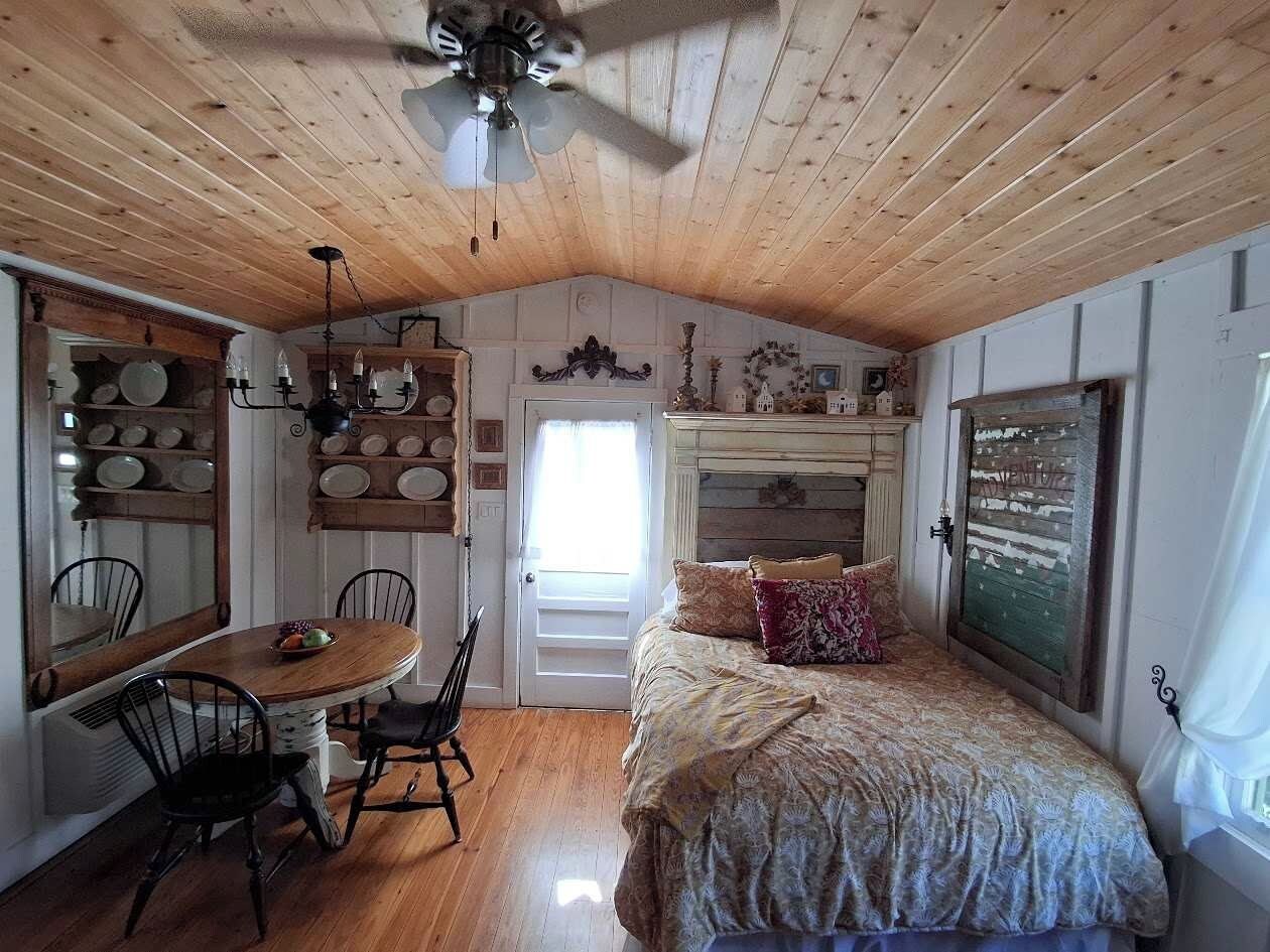 Une pièce avec un plafond en bois, un lit avec une literie à motifs, une table à manger avec des chaises et un lustre.