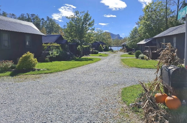 A gravel road leading to a row of cabins with a lake and mountains in the background.
