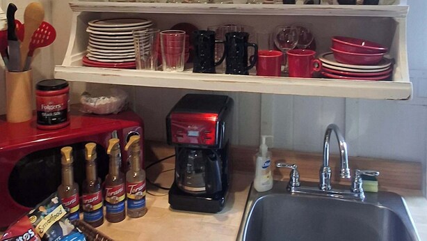 A kitchen with white shelves holding various dishes and glasses, a coffee maker, and a sink. - The Cedar Cabin | Lake Views, Walk to Cashiers (Cashiers)