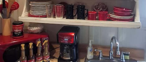 Une cuisine avec des étagères blanches où sont rangés différents plats et verres, une machine à café et un évier.