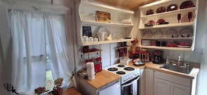 Una cocina compacta con gabinetes blancos, estufa, lavaplatos y estantes con platos y utensilios.
