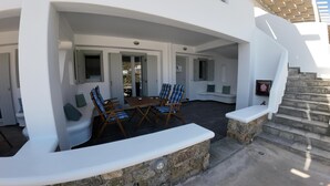 Un espace extérieur abrité, avec une table et des chaises, des marches en pierre et un banc.